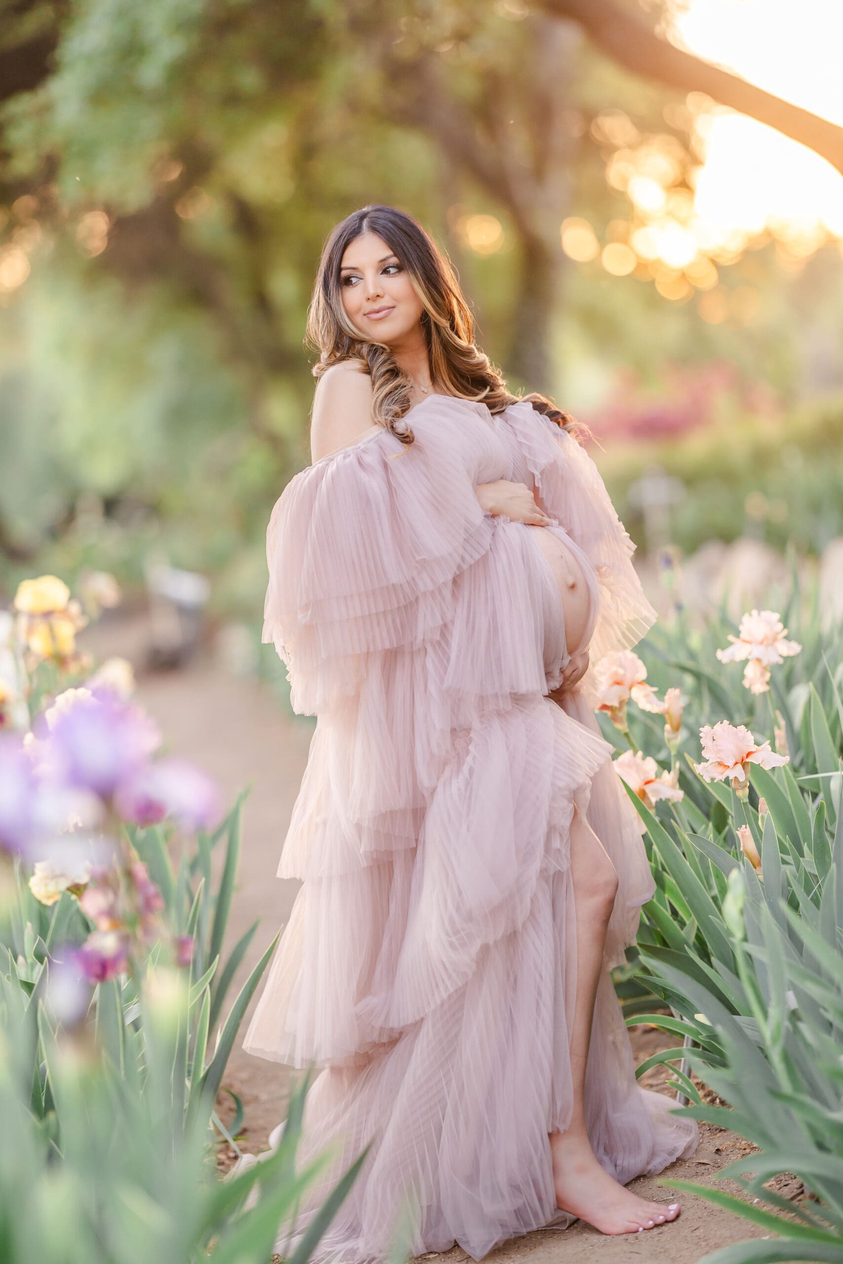 Bay Area family photographer Xio Ponce Bay Area Family Photographer photo of pregnat mom in a Irish garden with a pink dress posing with her belly out at golden hour.